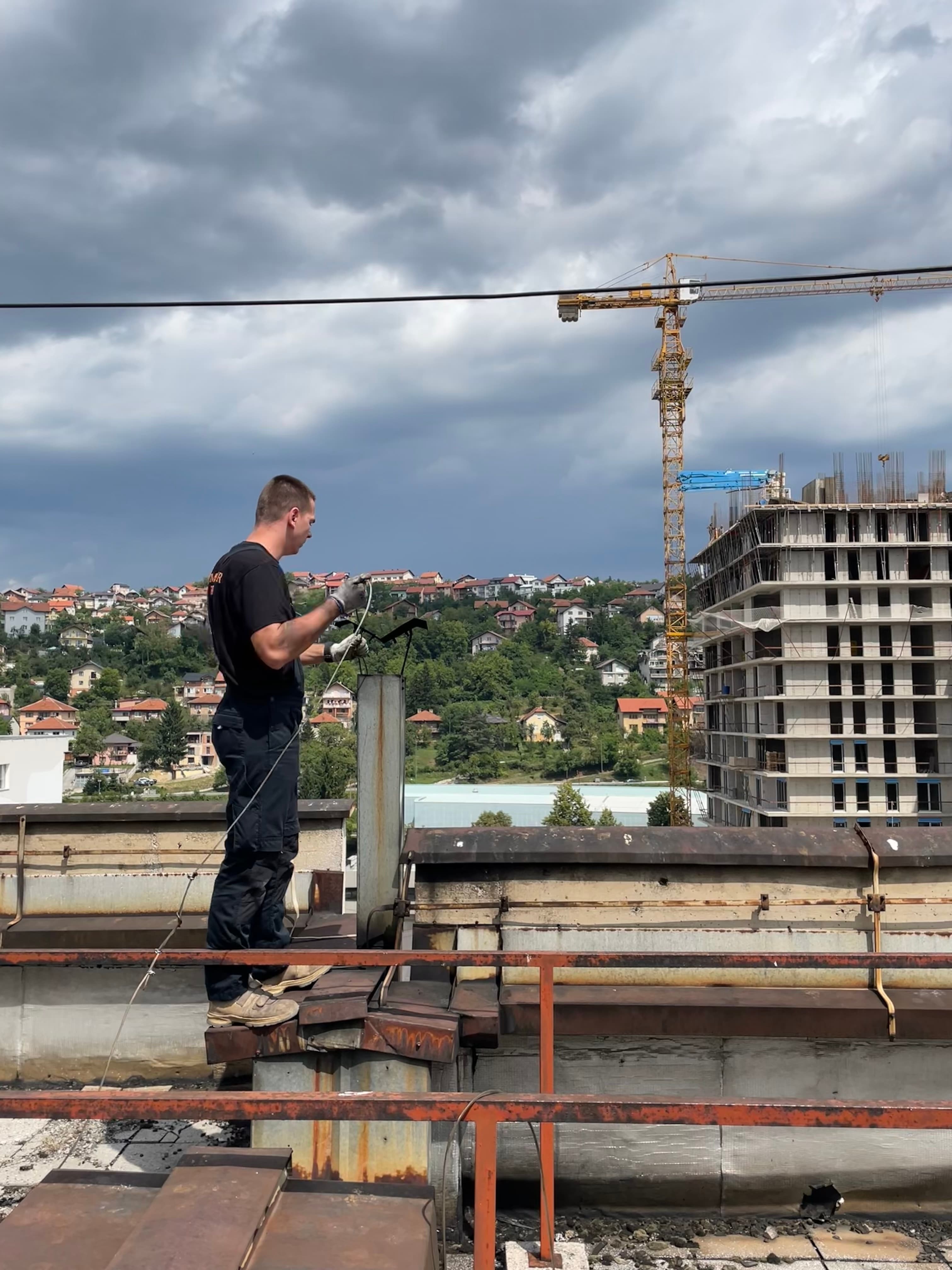 Dimnjačar Brkić čisti dimnjak na krovu zgrade u Sarajevu — pogled na grad